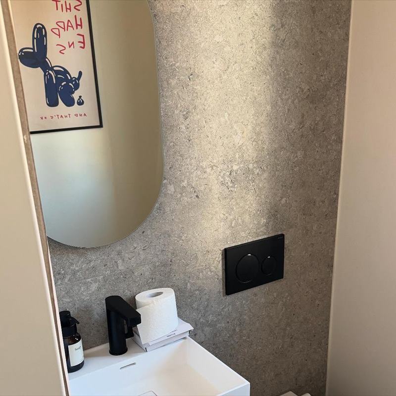 Gäste-WC mit rundem Spiegel und Wand in Steinoptik